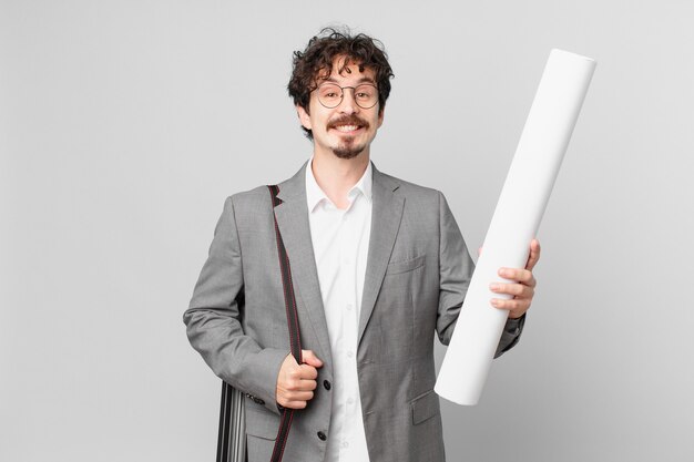 Joven arquitecto sonriendo felizmente con una mano en la cadera y confiado