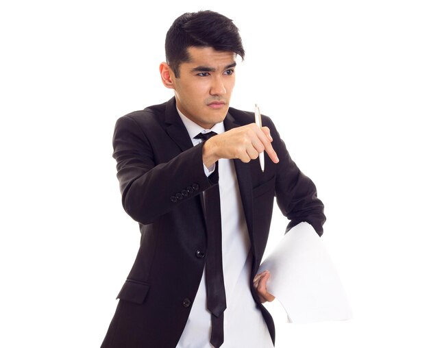 Joven arrogante con cabello negro en camisa blanca y traje negro con corbata con papeles