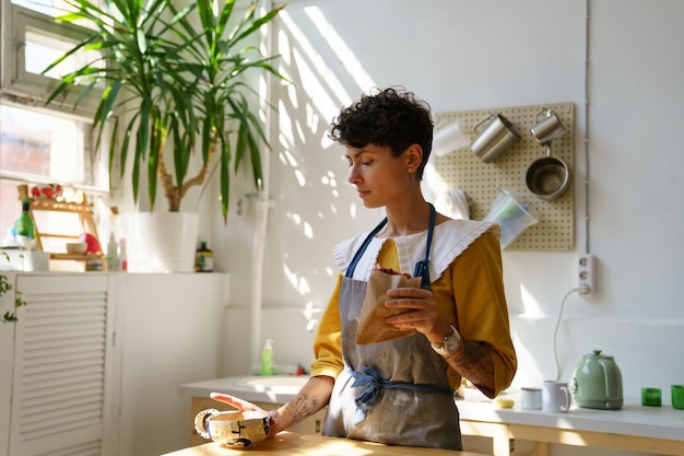 Joven artesana creativa que disfruta del desayuno mientras comienza a trabajar en su propio estudio de cerámica por la mañana