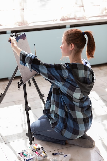 Foto la joven artista adolescente está sentada en el suelo de baldosas de mármol. mujer en proceso de pintura con pinturas al óleo.