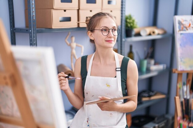 Joven artista caucásica sonriendo confiada dibujando en el estudio de arte