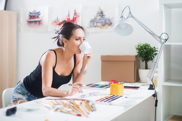 Joven artista dibujando una imagen de acuarela vista lateral sosteniendo una taza de café