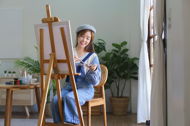 Joven artista femenina mezcla color en la paleta para pintar obras de arte en lienzo con disfrutar en el estudio en casa