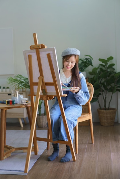 Joven artista femenina mezcla color en la paleta para pintar obras de arte en lienzo con disfrutar en el estudio en casa