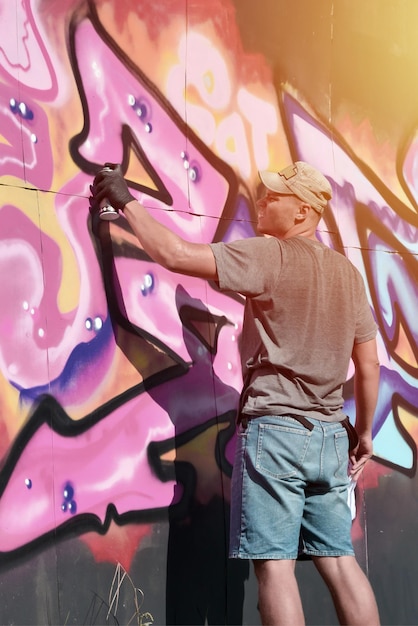 Foto joven artista de graffiti masculino caucásico dibujando una gran pintura de arte callejero en tonos azules y rosas