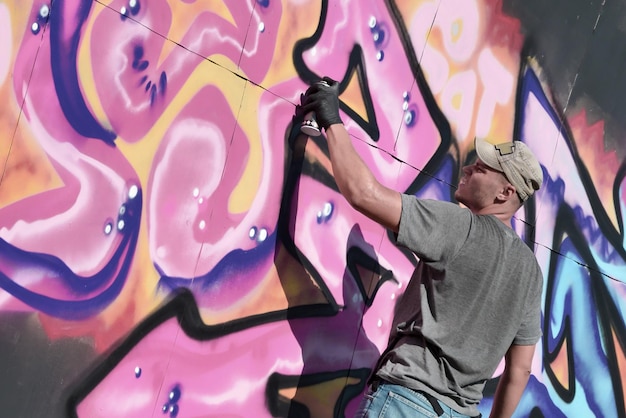 Joven artista de graffiti masculino caucásico dibujando una gran pintura de arte callejero en tonos azules y rosas