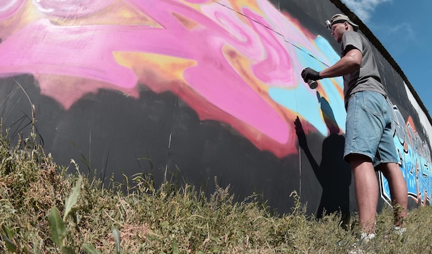 Joven artista de graffiti masculino caucásico dibujando una gran pintura de arte callejero en tonos azules y rosas