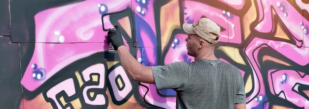 Joven artista de graffiti masculino caucásico dibujando una gran pintura de arte callejero en tonos azules y rosas