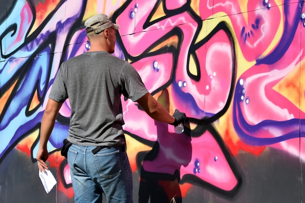 Joven artista de graffiti masculino caucásico dibujando una gran pintura de arte callejero en tonos azules y rosas