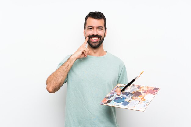 Joven artista hombre sosteniendo una paleta sobre aislado sonriendo con una expresión feliz y agradable