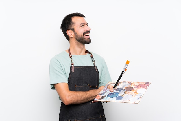 Joven artista hombre sosteniendo una paleta sobre fondo aislado feliz y sonriente