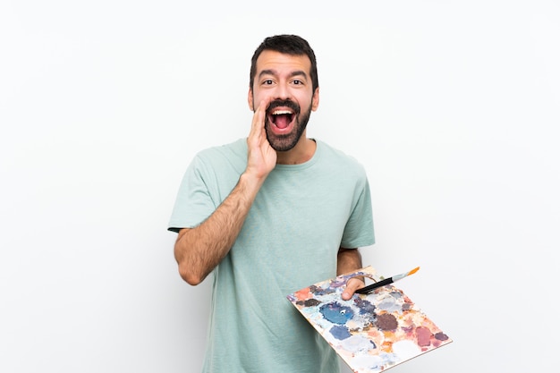 Joven artista hombre sosteniendo una paleta sobre fondo aislado gritando y anunciando algo