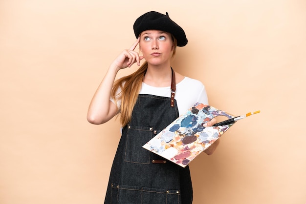 Joven artista mujer caucásica sosteniendo una paleta aislada en un fondo beige con dudas y pensando