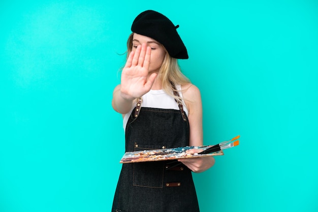 Joven artista mujer caucásica sosteniendo una paleta aislada sobre fondo azul haciendo gesto de parada y decepcionado