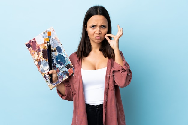 Joven artista mujer sosteniendo una paleta sobre fondo azul aislado que muestra un signo de gesto de silencio