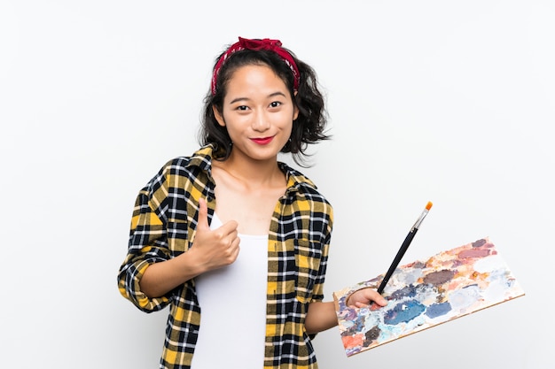 Joven artista mujer sosteniendo una paleta sobre fondo blanco aislado con los pulgares hacia arriba porque algo bueno ha sucedido