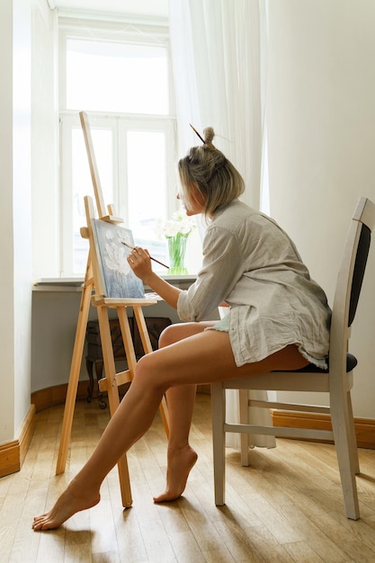 Joven artista pintando sobre lienzo en el caballete en el estudio de casa