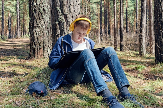 El joven artista se sienta en un bosque de pinos y pinta al aire libre y escucha música Día soleado ocio creativo