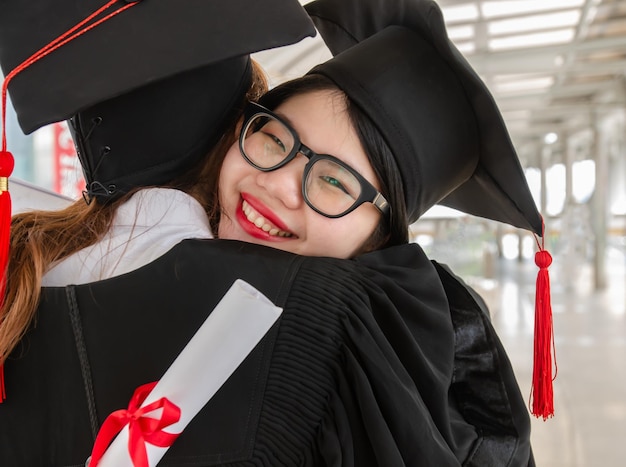 Joven asiática abrazando a su amiga y divirtiéndose después de recibir su certificado de graduación