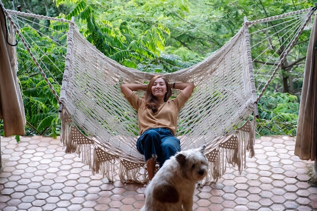 Una joven asiática acostada y relajada en una hamaca con un perro sentado cerca