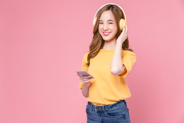 Una joven asiática alegre con auriculares escuchando música y disfrutando de su aplicación de lista de reproducción favorita en un smartphone con baile de fondo rosa