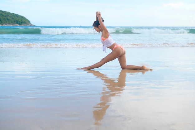 Joven asiática en bikini haciendo yoga en la playa concepto de salud y meditación