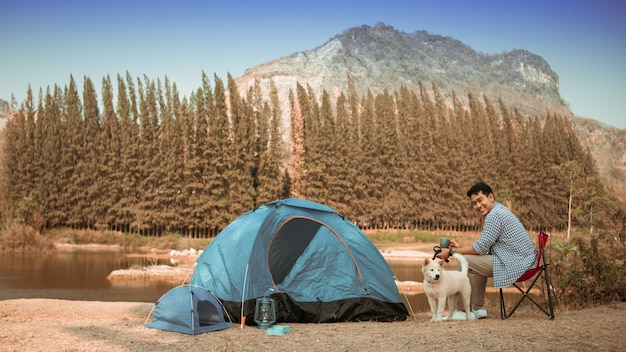 Joven asiática en camisa azul con lindo perrito acampando en la vista de la montaña de lake hill feliz y disfruta de la vida