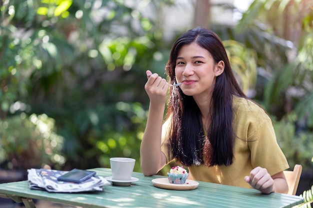 Joven asiática comiendo cupcake con café caliente en el jardín