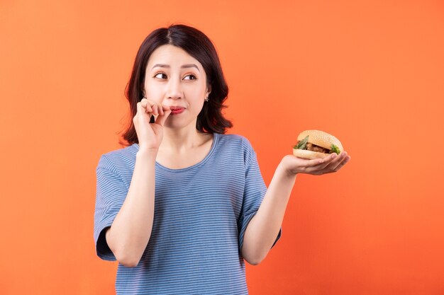 Joven asiática comiendo hamburguesa en naranja