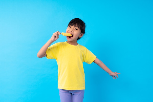 Joven asiática comiendo helado amarillo sobre azul