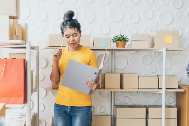 joven asiática comprobando mercancías en el estante de stock en el almacén