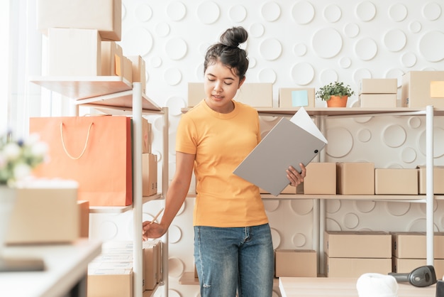 joven asiática comprobando mercancías en el estante de stock en el almacén