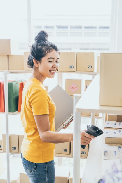 joven asiática comprobando mercancías en el estante de stock en el almacén