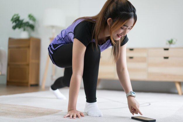 Joven asiática comprobando el tiempo de entrenamiento en un teléfono inteligente mientras hace ejercicio con un estilo de vida saludable