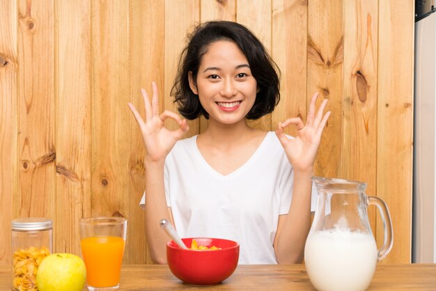 Joven asiática desayunando leche mostrando un signo bien con los dedos