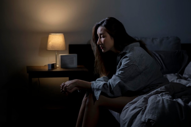 Joven asiática en el dormitorio sintiéndose triste cansada y preocupada sufriendo depresión en salud mental mujer sentada en la cama no puede dormir de insomnio
