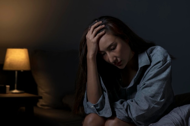 Joven asiática en el dormitorio sintiéndose triste cansada y preocupada sufriendo depresión en salud mental mujer sentada en la cama no puede dormir de insomnio