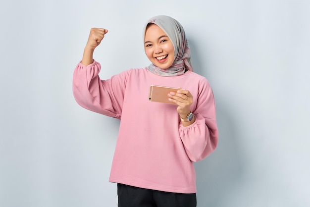 Una joven asiática emocionada con camisa rosa usando un teléfono móvil recibió buenas noticias aisladas sobre fondo blanco