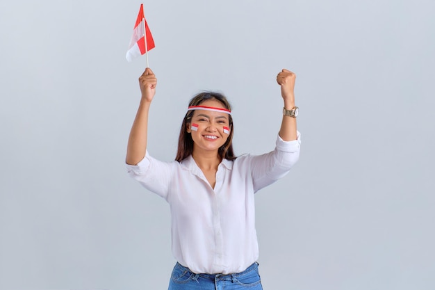 Una joven asiática emocionada celebra el día de la independencia de Indonesia sosteniendo la bandera de Indonesia aislada de fondo blanco