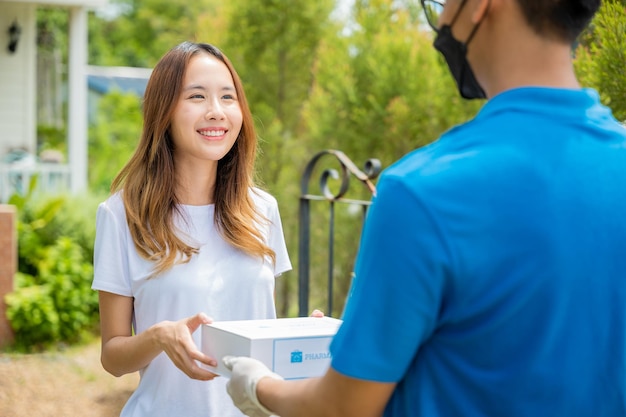 Una joven asiática enferma recibe una caja de farmacia de primeros auxilios del servicio de entrega del hospital, una mujer feliz que recibe un medicamento para el paciente del repartidor, un concepto de medicina de la salud en línea