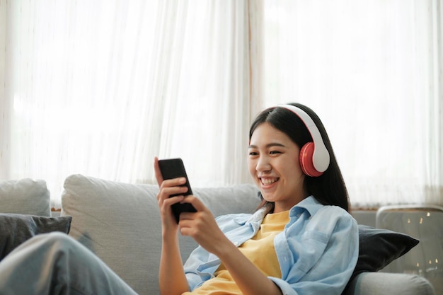 Joven asiática escuchando música usando un teléfono inteligente en casa