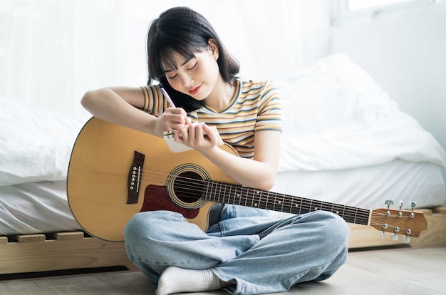 Joven asiática está practicando guitarra en casa y componiendo música