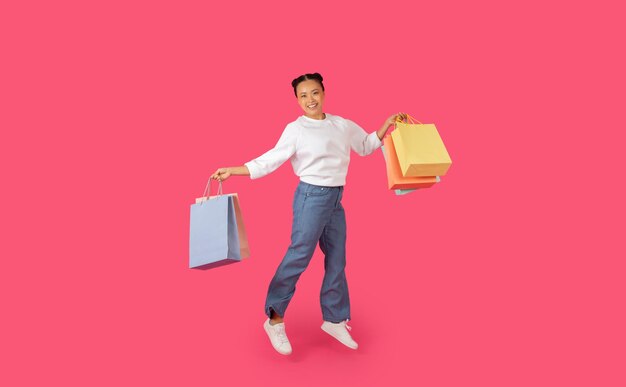 Una joven asiática está saltando en el aire con dos bolsas de compras en sus manos.