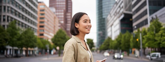 Foto joven asiática explorando la ciudad con una aplicación para teléfonos inteligentes sosteniendo un teléfono móvil y caminando por la calle