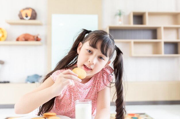 Una joven asiática feliz come galletas de leche con leche fresca para el desayuno en la mañana