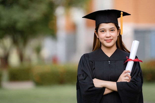 Una joven asiática feliz graduada universitaria en toga de graduación y birrete tiene un certificado de grado que celebra los logros educativos en el campus universitario. Educación foto de stock