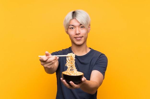 Joven asiática con fideos sobre amarillo aislado