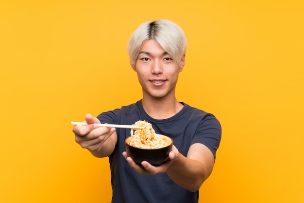 Joven asiática con fideos sobre amarillo aislado