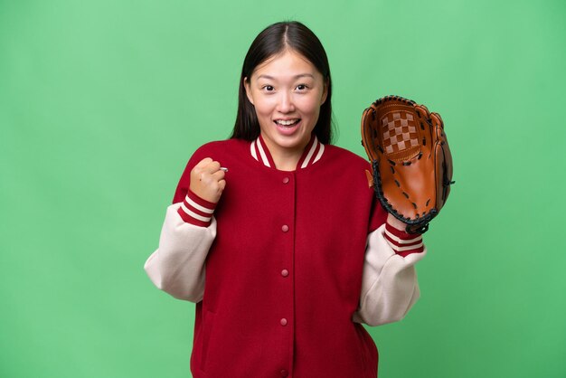 Joven asiática con guante de béisbol sobre un fondo aislado celebrando una victoria en posición ganadora