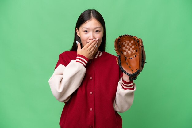 Joven asiática con guante de béisbol sobre un fondo aislado feliz y sonriente cubriendo la boca con la mano